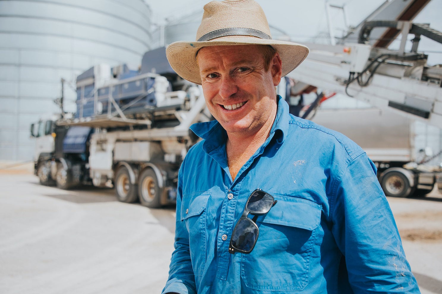 A smiling man in a hat standing by a two large silos