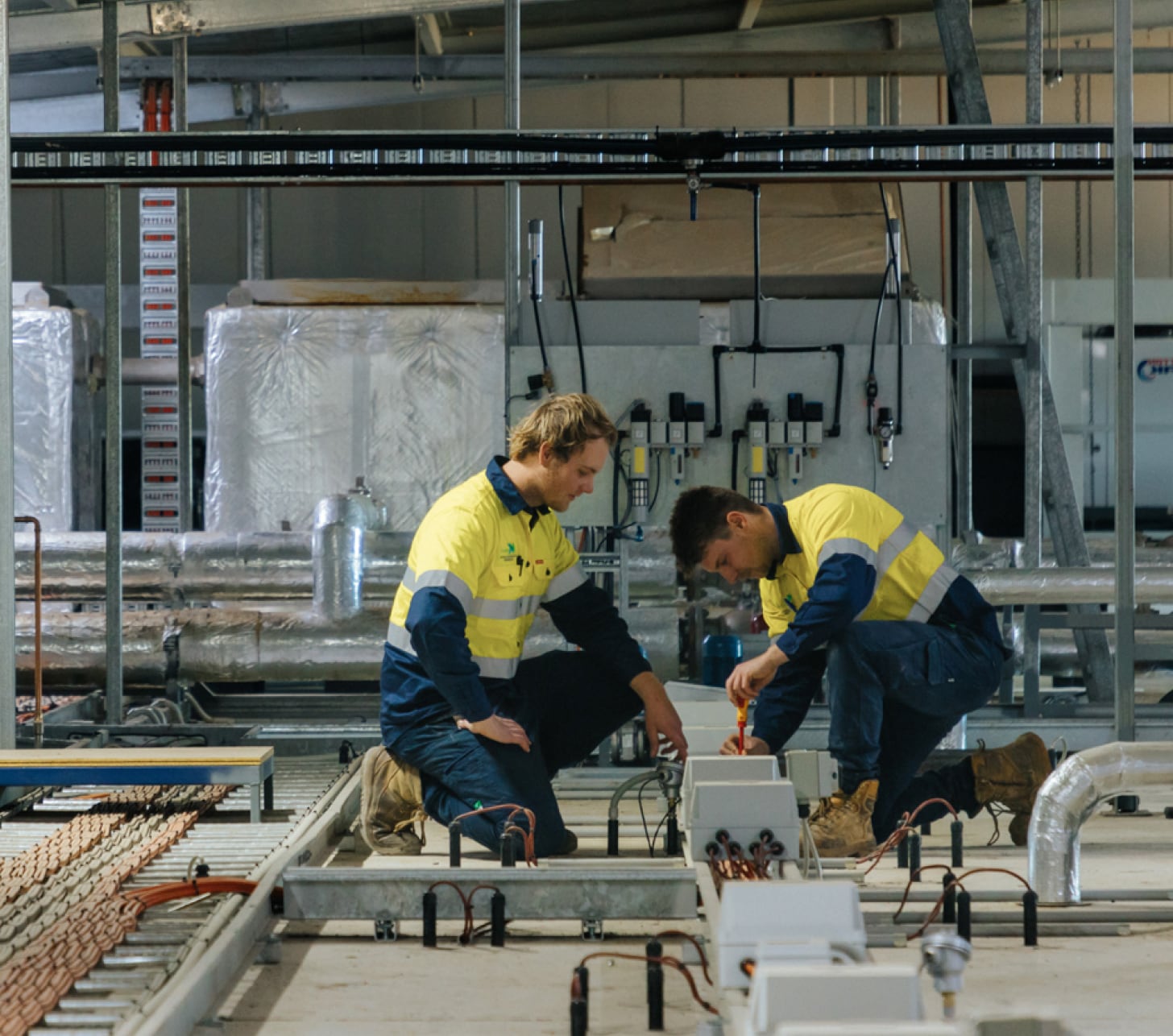Two men work on electrical equipment on a factory floor